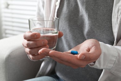 Man with glass of water and pill on blurred background, closeup