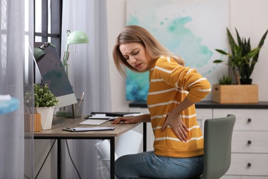 Photo of Young woman suffering from back pain in office