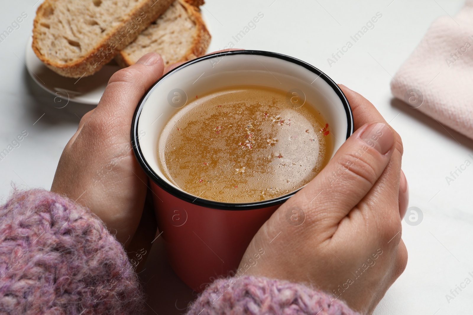 Photo of Woman with cup of hot delicious bouillon at white marble table, closeup