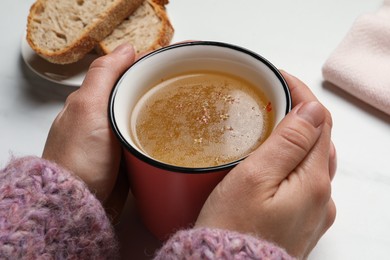 Woman with cup of hot delicious bouillon at white marble table, closeup