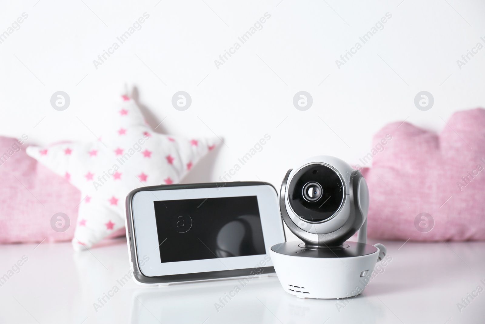 Photo of Modern CCTV security camera, monitor and decorative nursery pillows on table against white background. Space for text