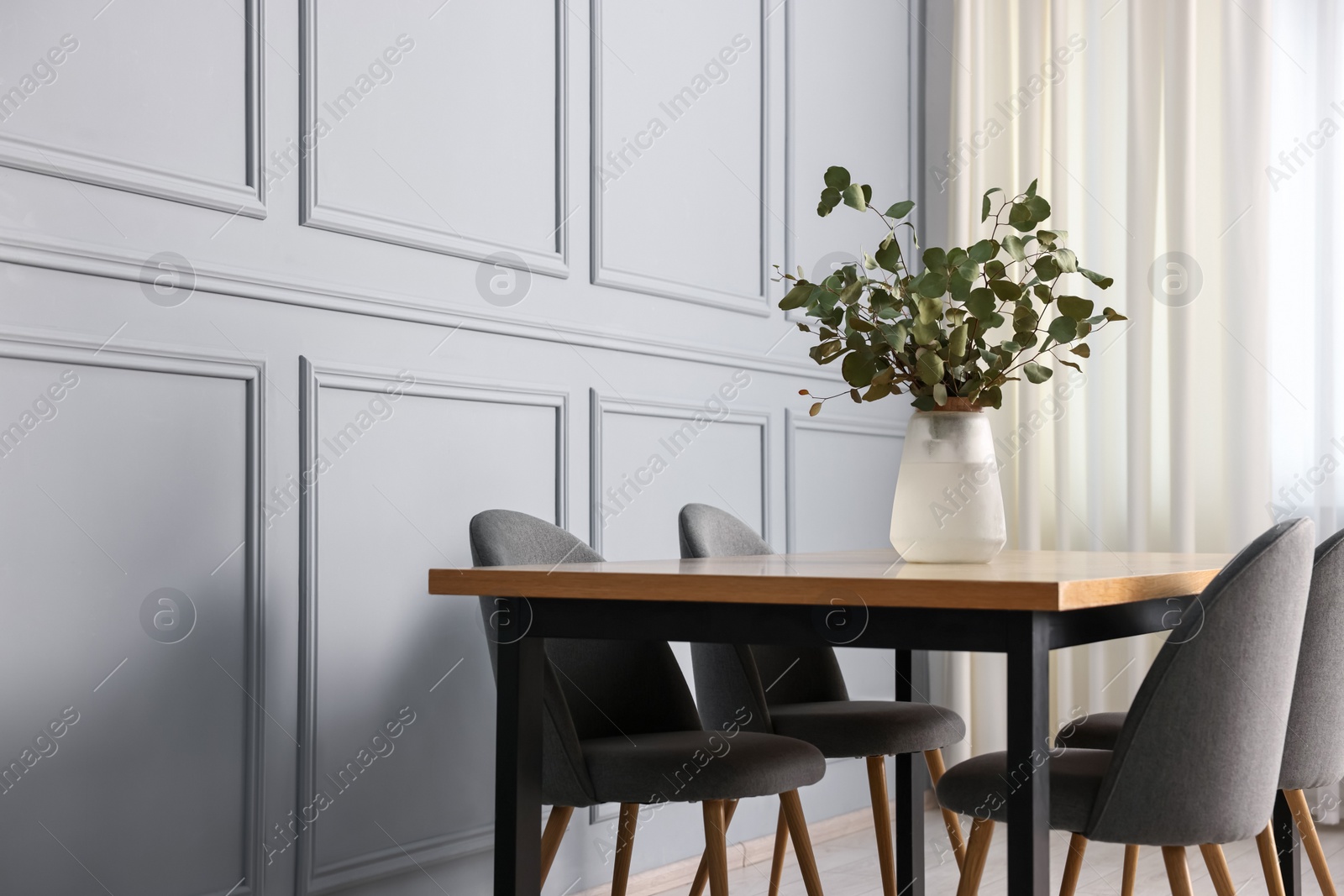 Photo of Soft chairs, table and vase with eucalyptus branches in stylish dining room. Space for text