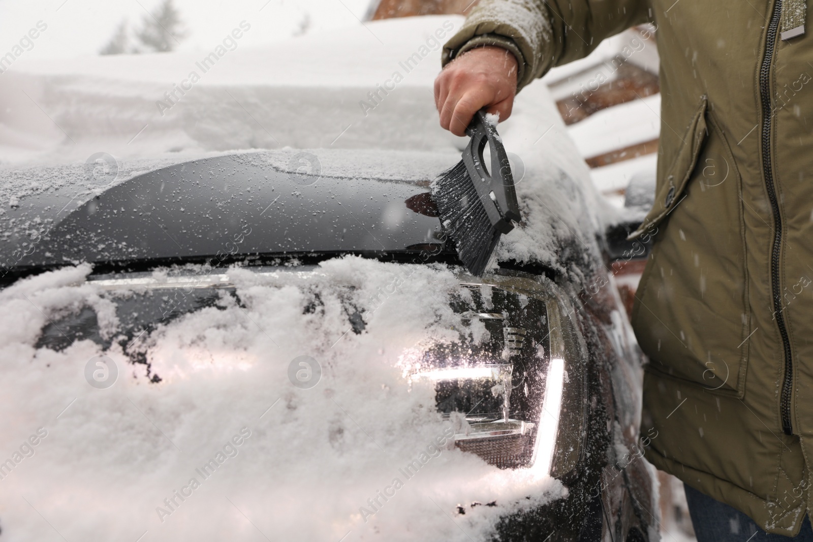 Photo of Young man cleaning snow from car outdoors on winter day, closeup