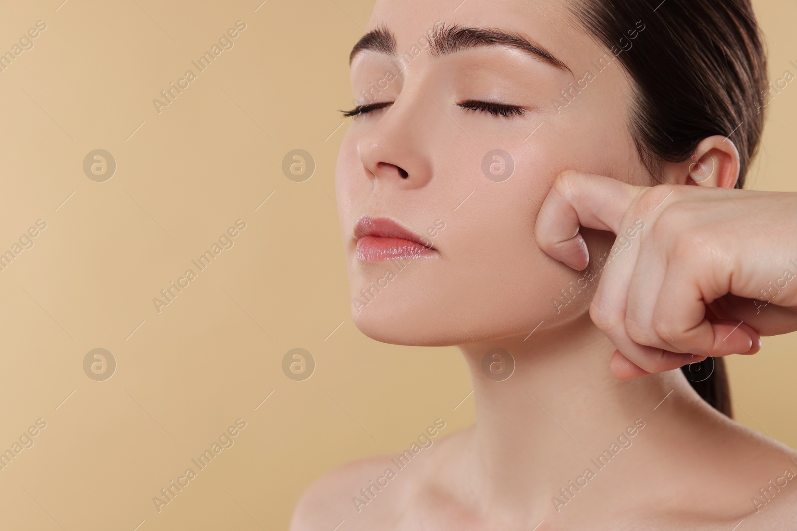 Photo of Young woman massaging her face on beige background. Space for text