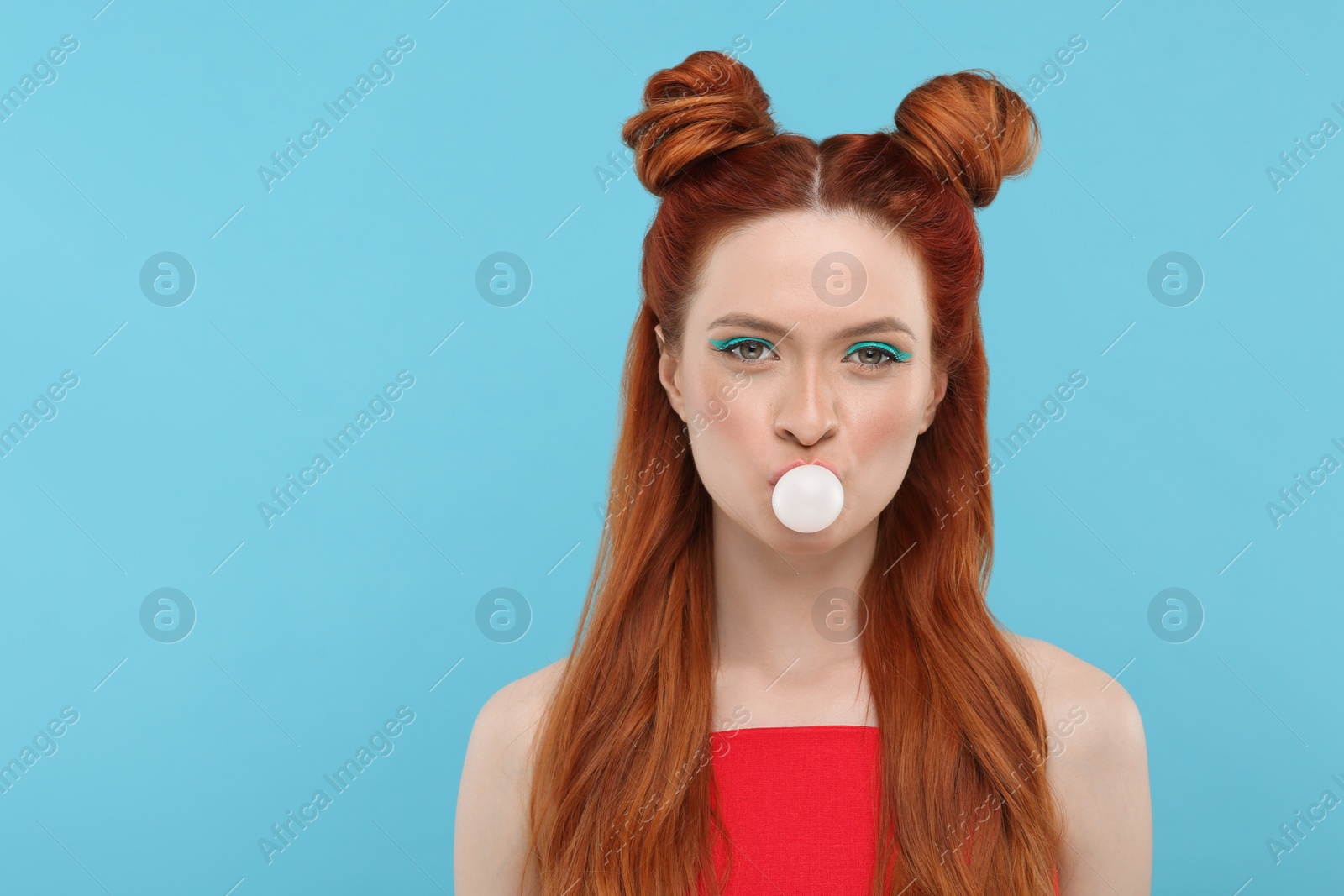 Photo of Portrait of beautiful woman with bright makeup blowing bubble gum on light blue background. Space for text