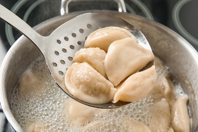 Photo of Closeup of dumplings on skimmer over stewpan with boiling water. Home cooking