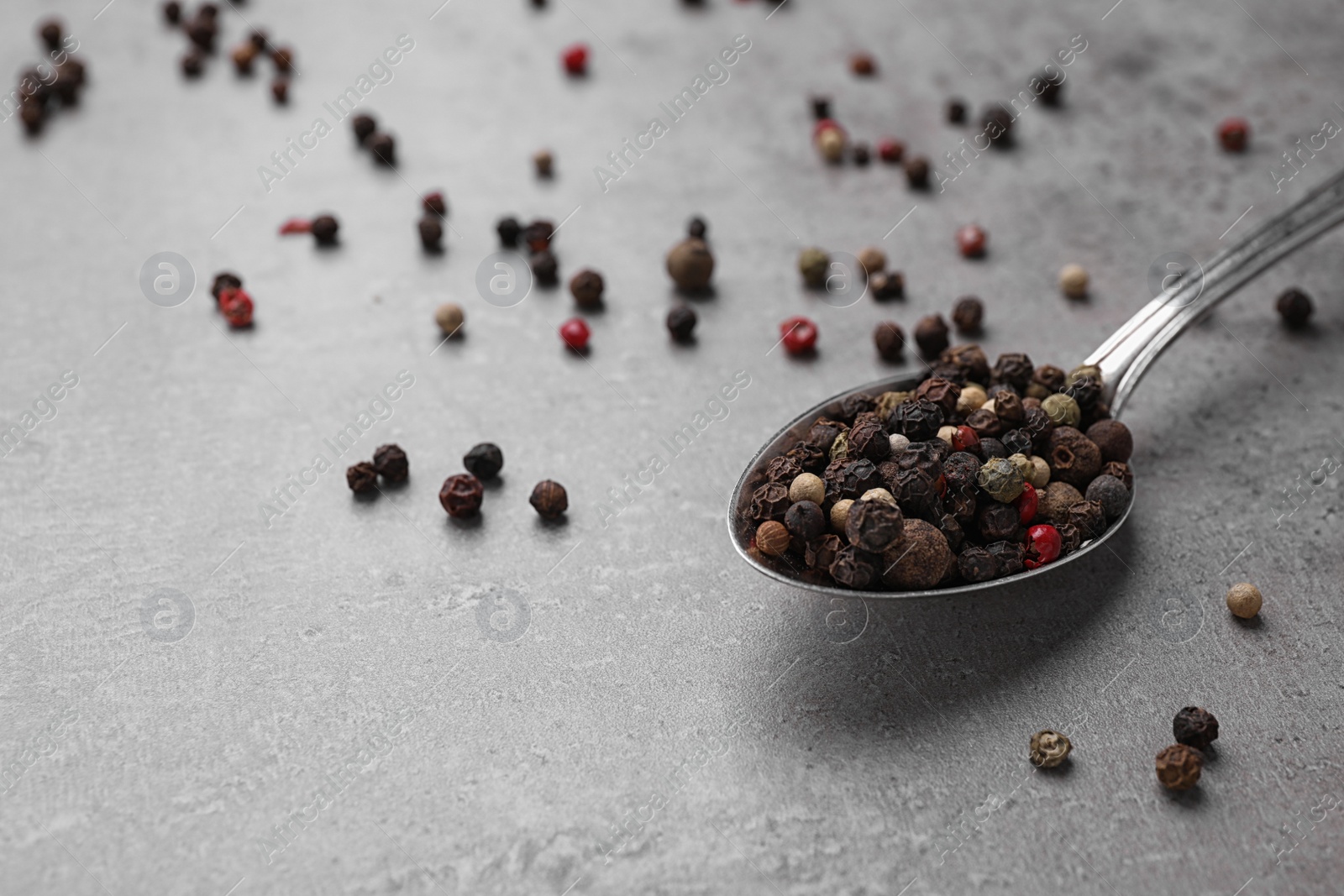 Photo of Spoon with mixed peppercorns on grey table, closeup