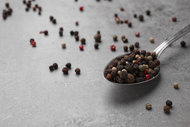 Spoon with mixed peppercorns on grey table, closeup