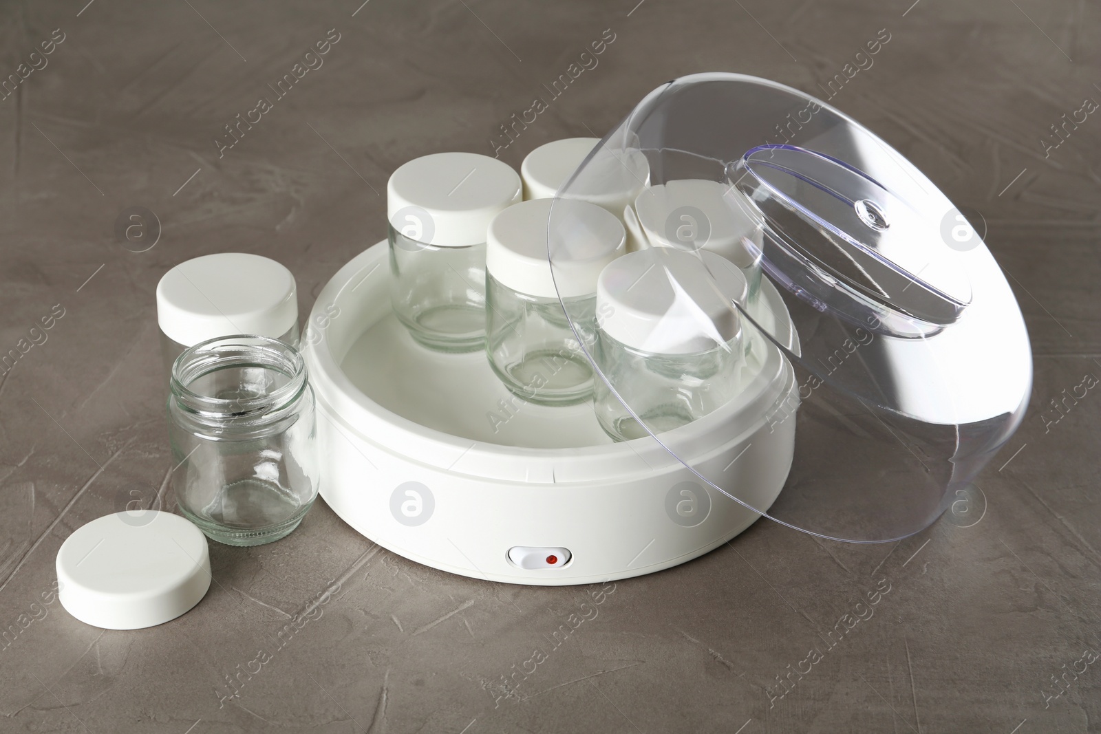 Photo of Modern yogurt maker with empty jars on grey table