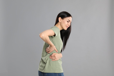 Photo of Woman suffering from lower back pain on light grey background. Visiting orthopedist