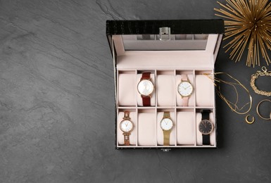 Jewelry box with stylish wristwatches and golden accessories on black table, flat lay. Space for text