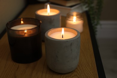 Lit candles in different holders on wooden table indoors