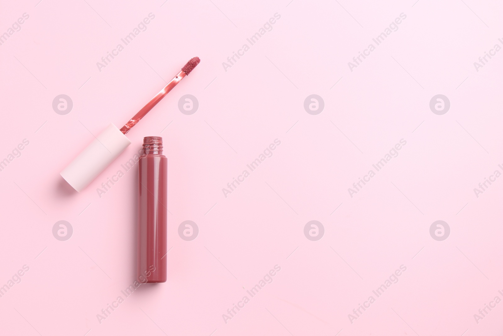 Photo of Bright lip gloss and applicator on pink background, top view. Space for text