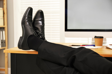 Photo of Lazy employee resting at table in office, closeup of legs