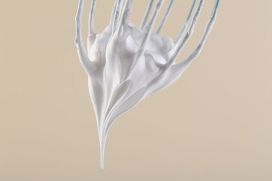 Photo of Whisk with whipped cream on beige background, closeup