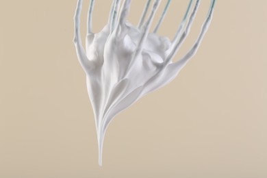 Whisk with whipped cream on beige background, closeup