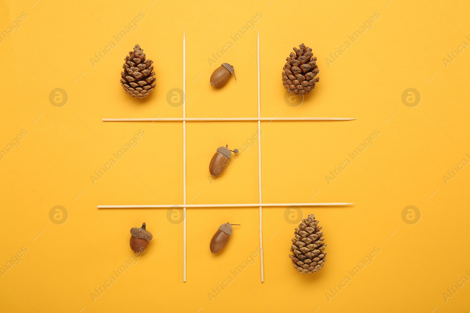 Photo of Tic tac toe game made with acorns and pine cones on yellow background, top view