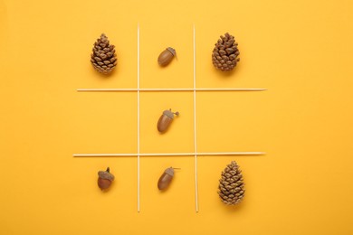 Tic tac toe game made with acorns and pine cones on yellow background, top view