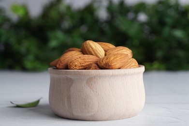 Photo of Tasty almonds in wooden bowl on white table