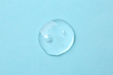 Drop of cosmetic serum on light blue background, top view