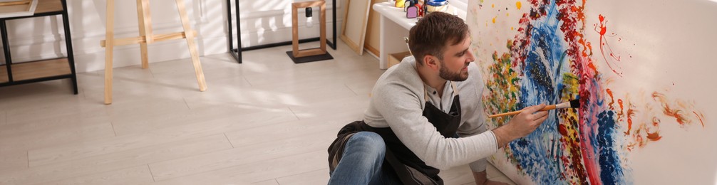 Image of Young man painting on canvas with brush in artist studio. Banner design