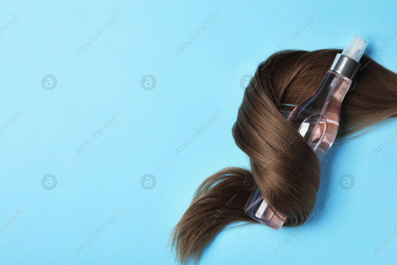 Photo of Spray bottle wrapped in lock of hair on light blue background, flat lay with space for text. Natural cosmetic products