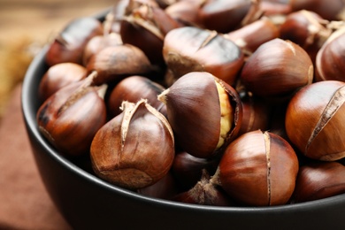 Delicious roasted edible chestnuts in bowl on table, closeup