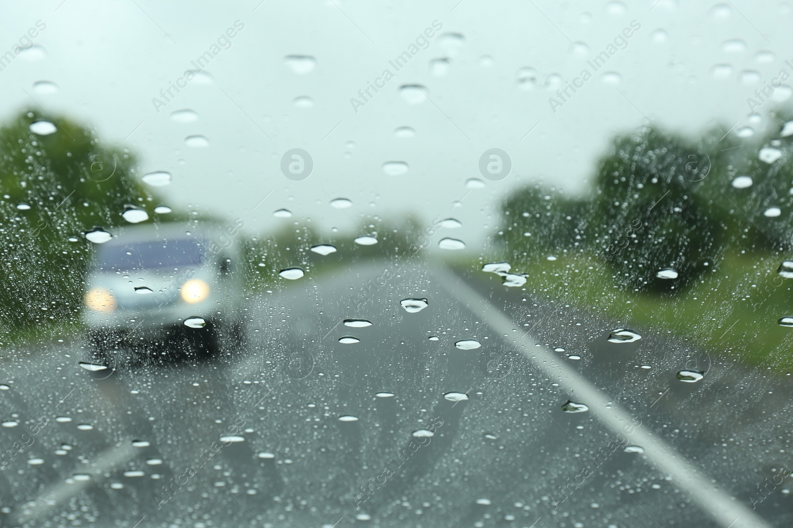 Photo of Blurred view of country road through wet car window. Rainy weather