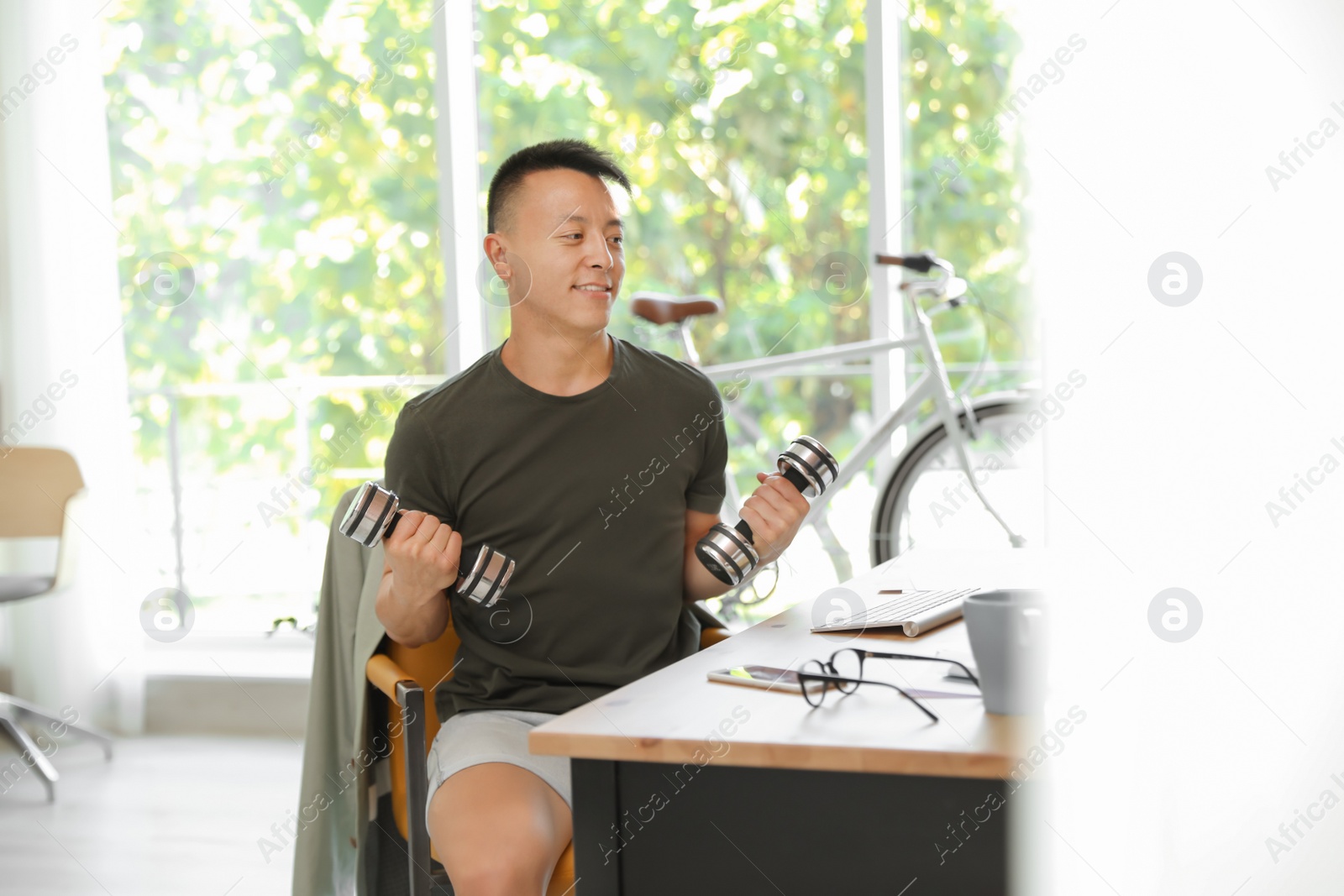 Photo of Young man lifting weights in office. Workplace fitness