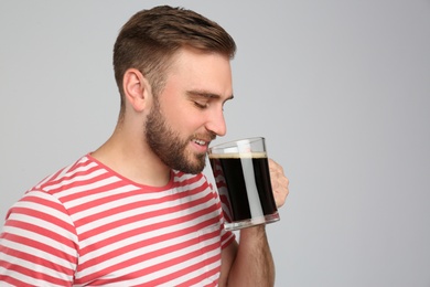 Photo of Handsome man with cold kvass on light grey background. Traditional Russian summer drink