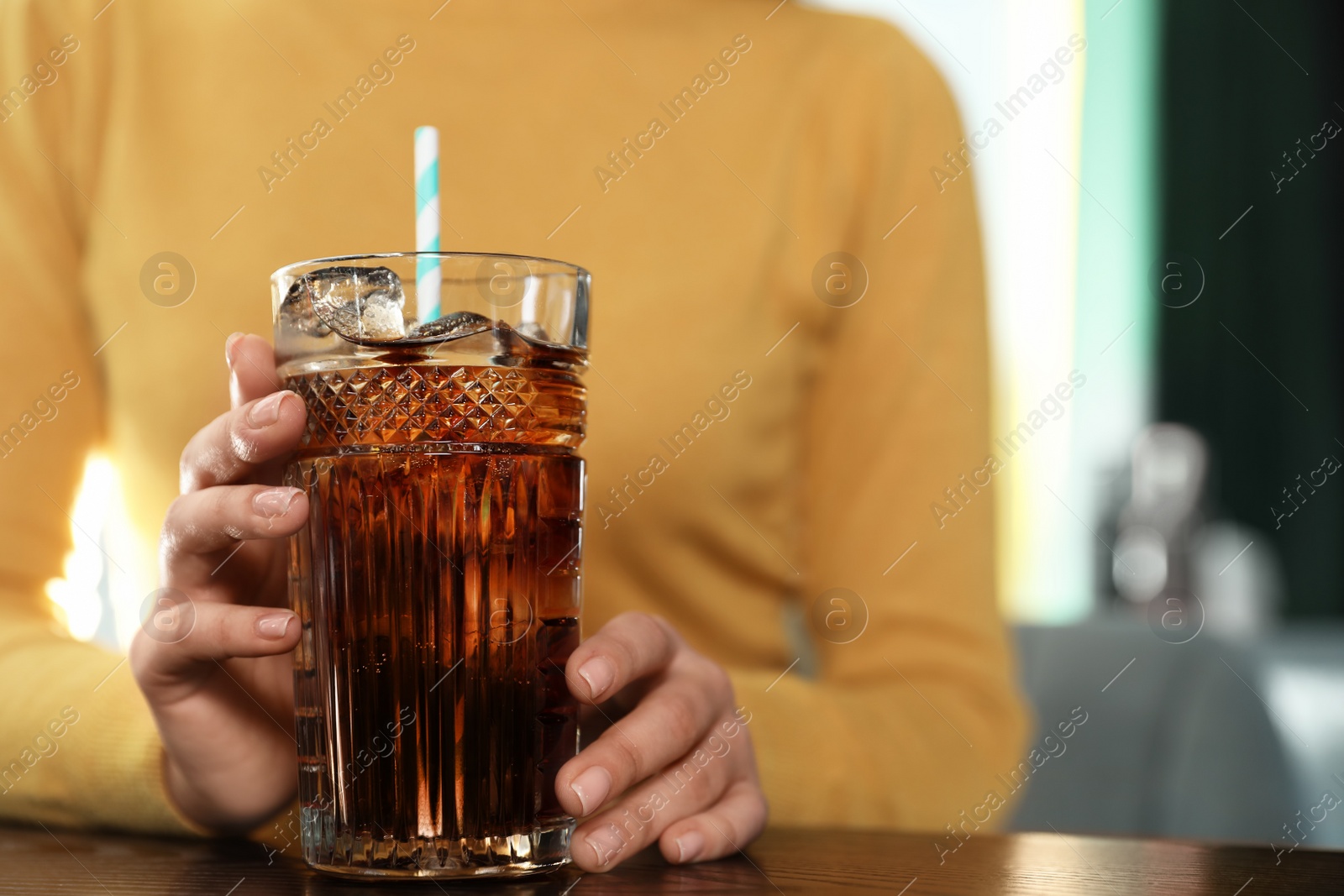 Photo of Woman with glass of refreshing cola at table indoors, closeup. Space for text