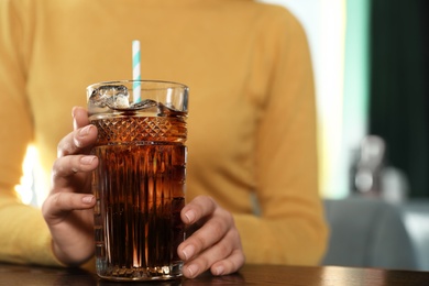 Woman with glass of refreshing cola at table indoors, closeup. Space for text