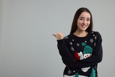 Photo of Happy young woman in Christmas sweater pointing at something on grey background. Space for text