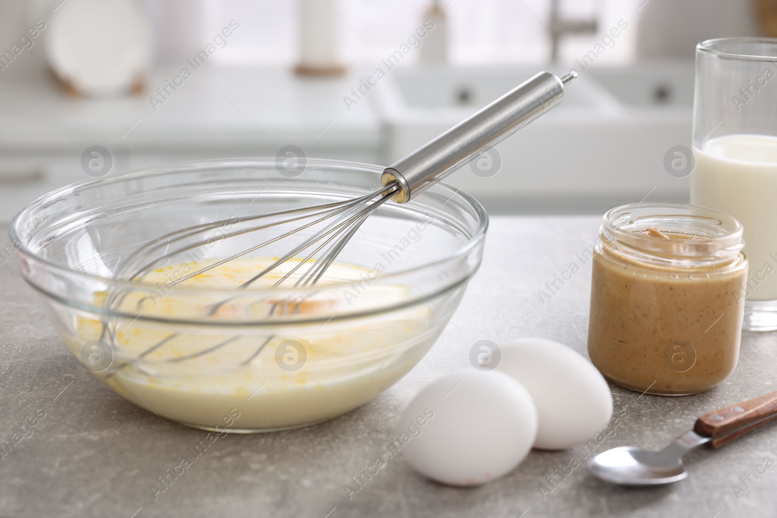 Photo of Whisk, bowl, beaten eggs and other ingredients on grey table indoors