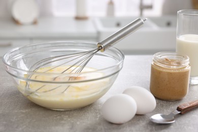 Whisk, bowl, beaten eggs and other ingredients on grey table indoors