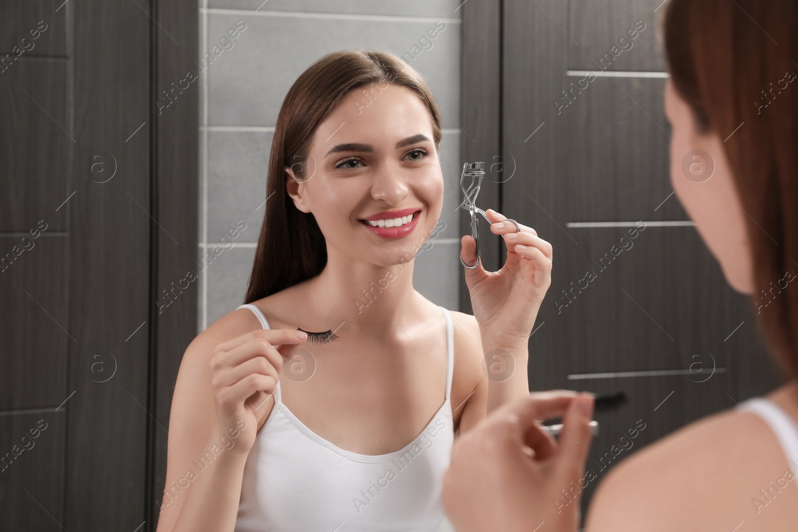 Photo of Woman with curler and false eyelashes near mirror indoors