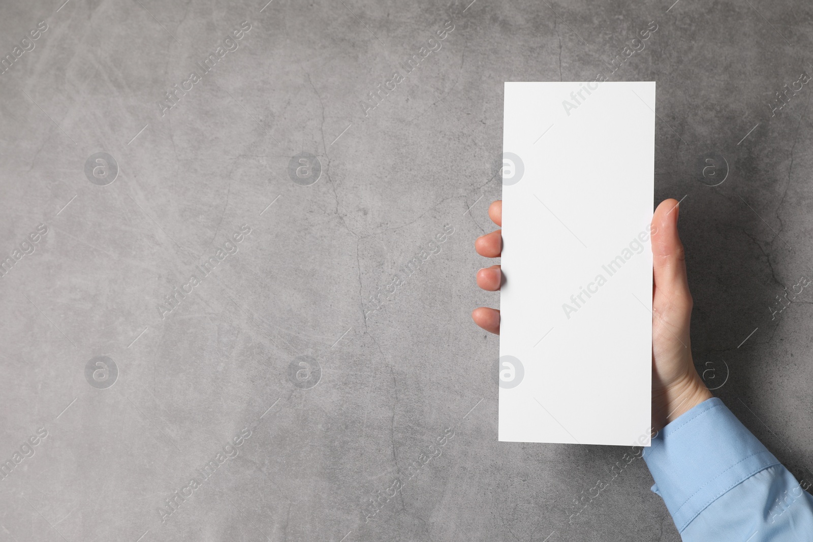 Photo of Woman holding blank card at grey table, top view. Mockup for design