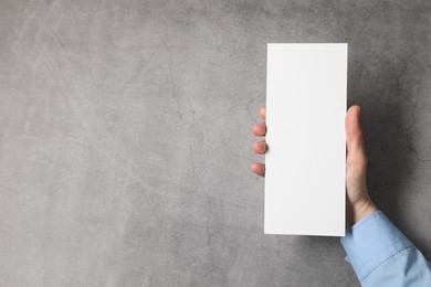 Photo of Woman holding blank card at grey table, top view. Mockup for design