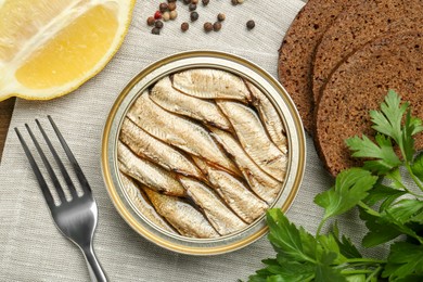 Tin can with tasty sprats served on table, flat lay