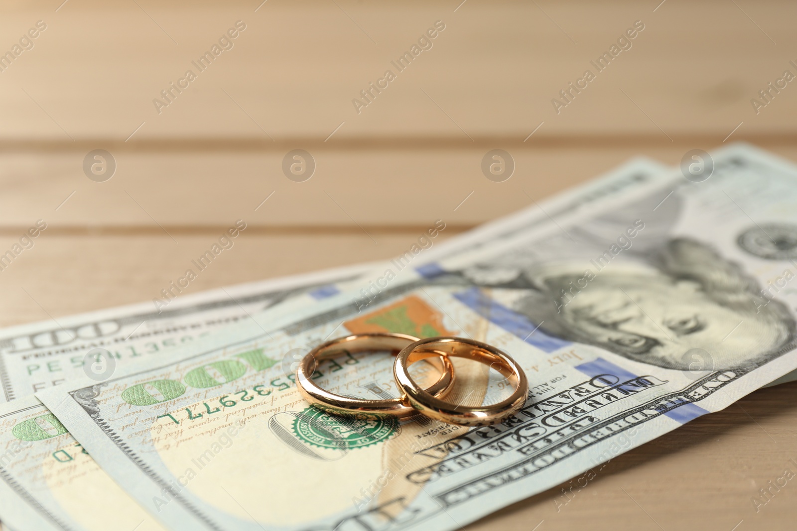 Photo of Honeymoon concept. Dollar banknotes and golden rings on wooden table, closeup
