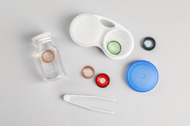 Photo of Different color contact lenses, tweezers and containers on light background, flat lay