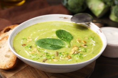 Photo of Delicious broccoli cream soup with basil and pumpkin seeds served on wooden table, closeup