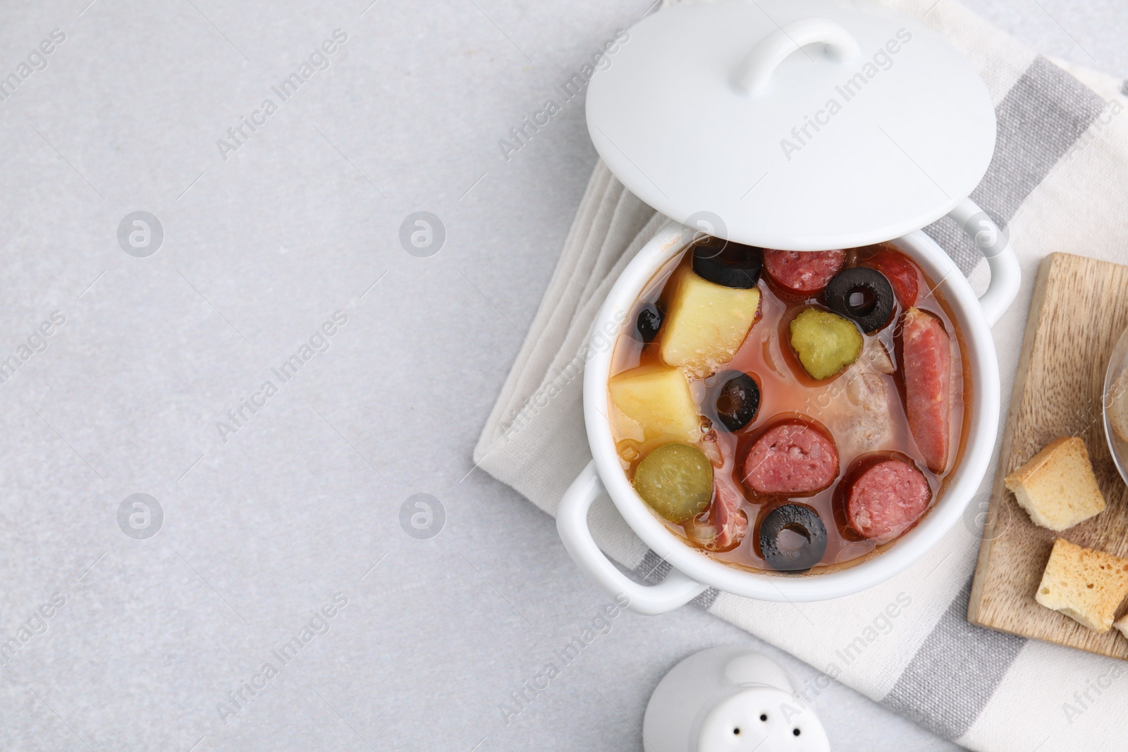 Photo of Meat solyanka soup with thin dry smoked sausages in pot on light table, flat lay. Space for text