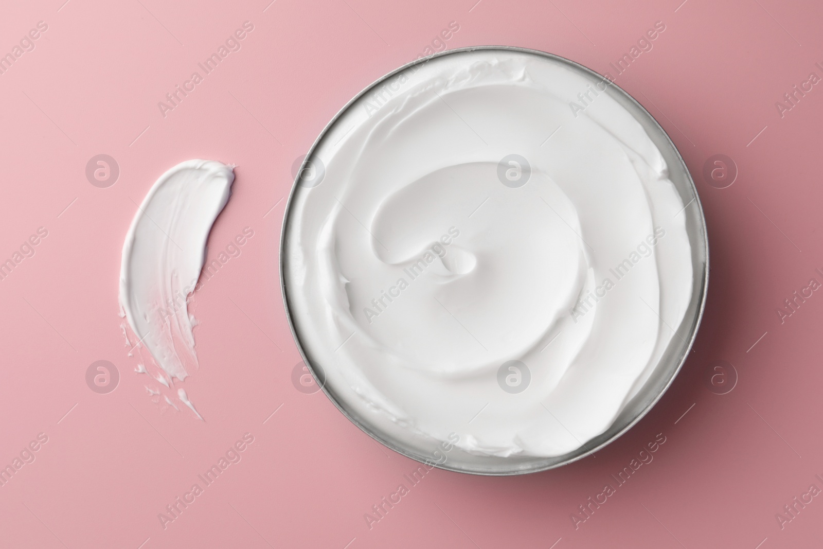 Photo of Jar of face cream and sample on pink background, flat lay