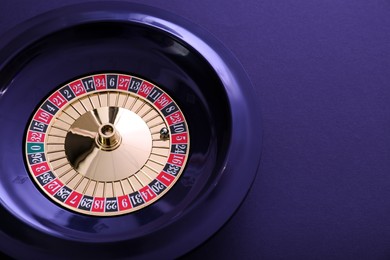 Photo of Roulette wheel with ball on dark violet background, top view and space for text. Casino game