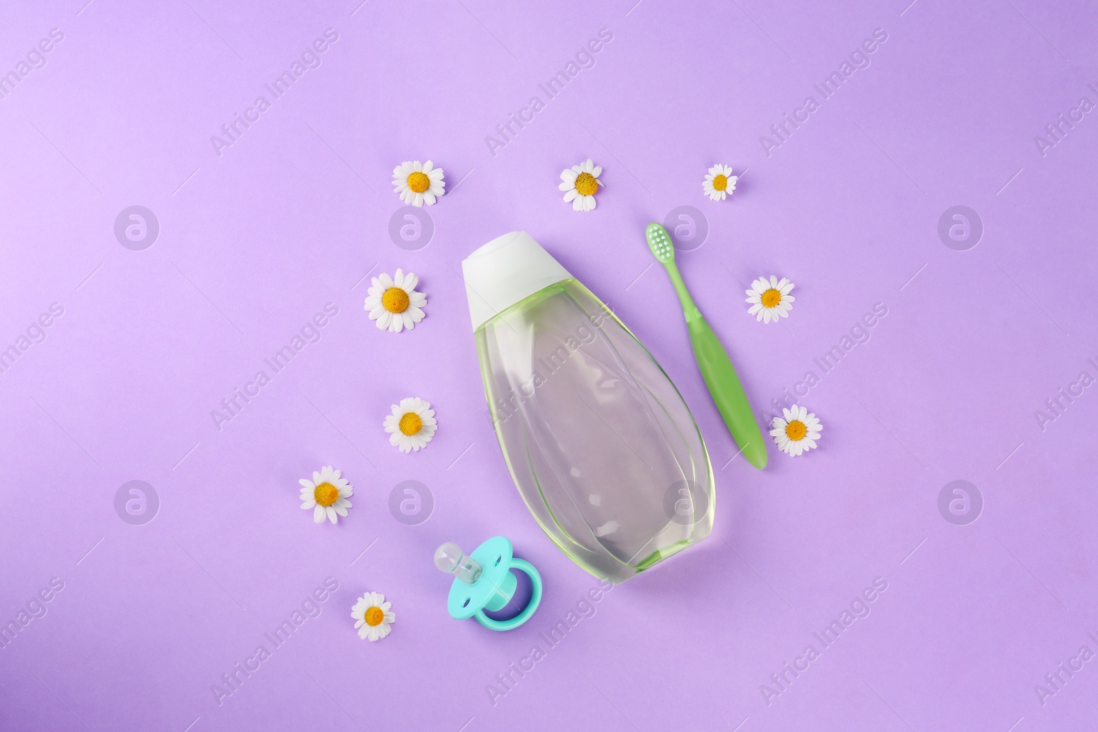 Photo of Bottle with baby oil, pacifier and toothbrush near daisies on violet background, flat lay