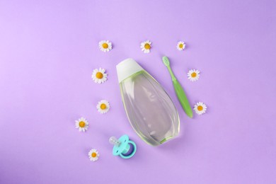 Photo of Bottle with baby oil, pacifier and toothbrush near daisies on violet background, flat lay