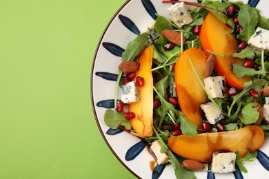 Photo of Tasty salad with persimmon, blue cheese, pomegranate and almonds served on light green background, top view. Space for text