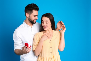 Man with engagement ring making marriage proposal to girlfriend on blue background