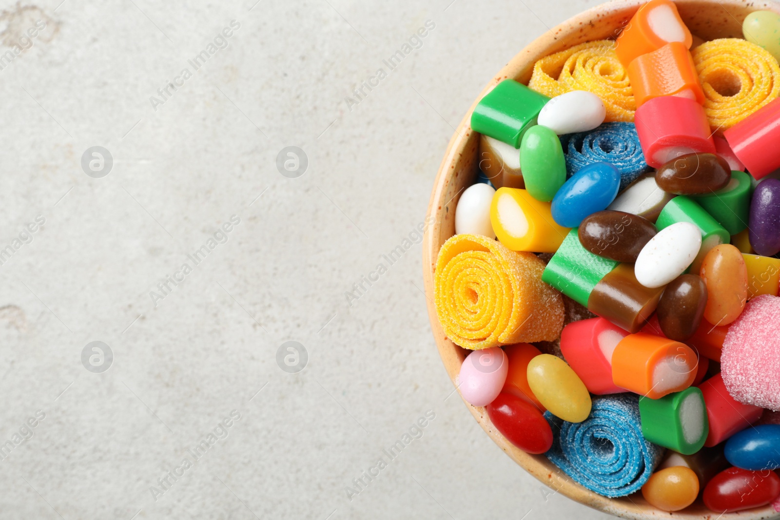 Photo of Bowl of delicious colorful candies on gray table, top view with space for text